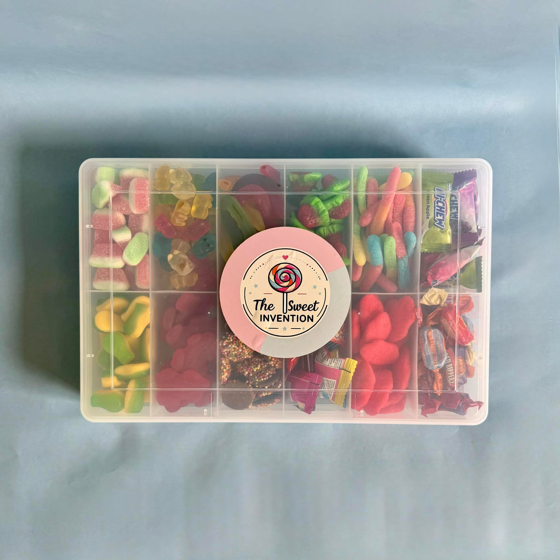Clear container with assorted gummy candies and a 'The Sweet Invention' label on a light blue background